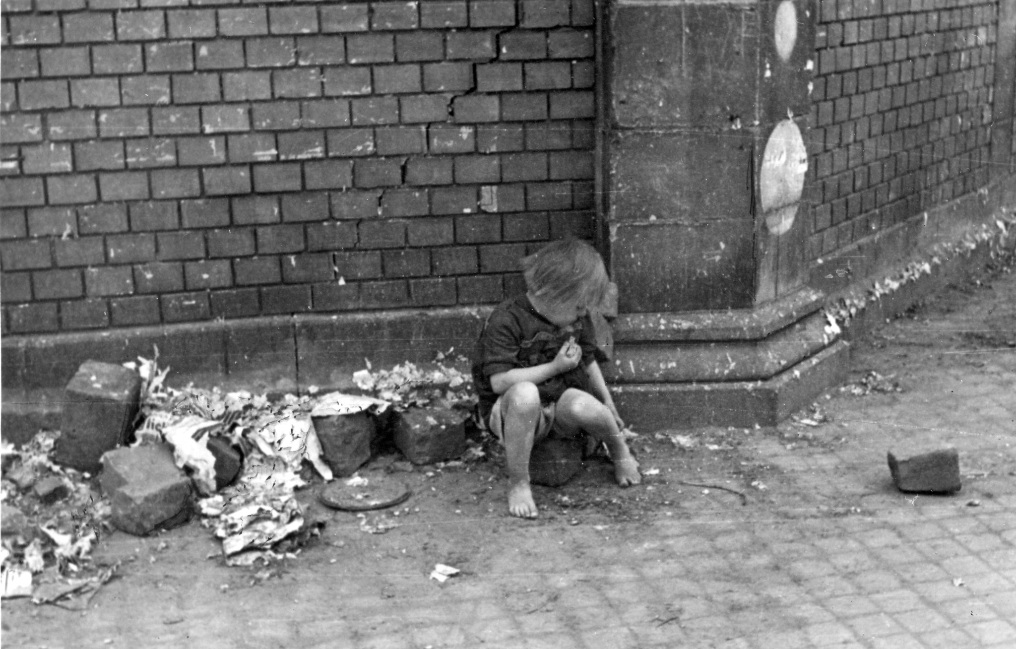 Ein kleines Kind sitzt an einer schmutzigen Strassenecke