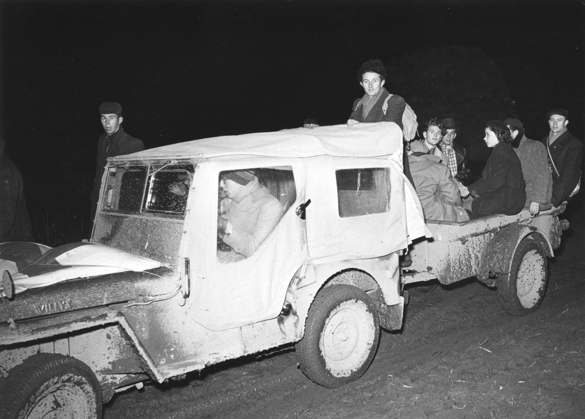 Ein Mann fährt einen Jeep, auf dem Anhänger sitzen mehrere Jugendliche