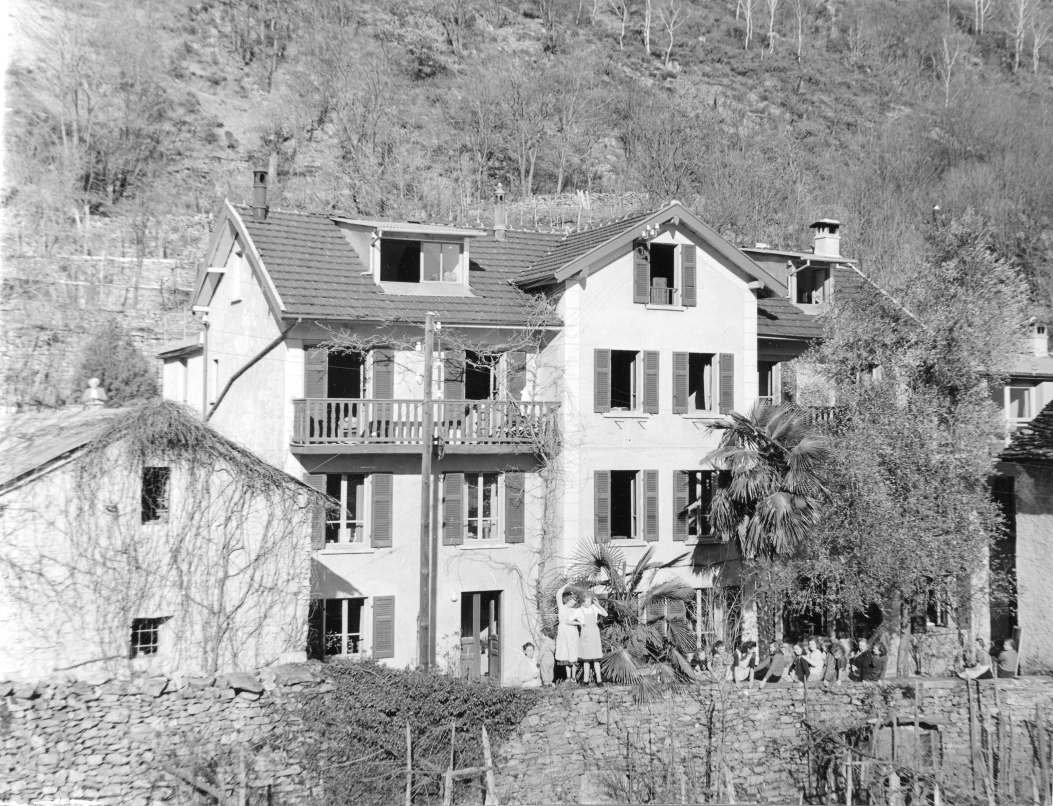 Alle Fenster einer Hauses sind geöffnet, im Garten winken die Schülerinnen der Hauswirtschaftschule