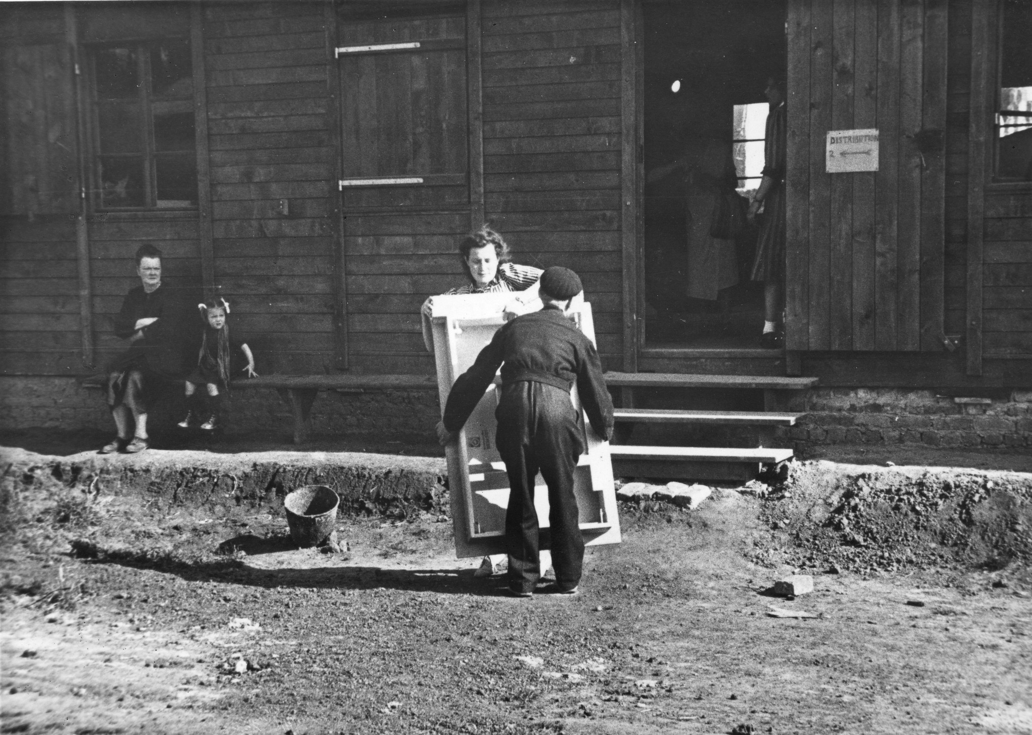 "Fives [Stadtviertel von Lille, Nord-Pas-de-Calais] Möbelverteilung", eine Frau und ein Mann tragen einen Möbelstück, vermutlich im SAH-Sozialzentrum, um 1946