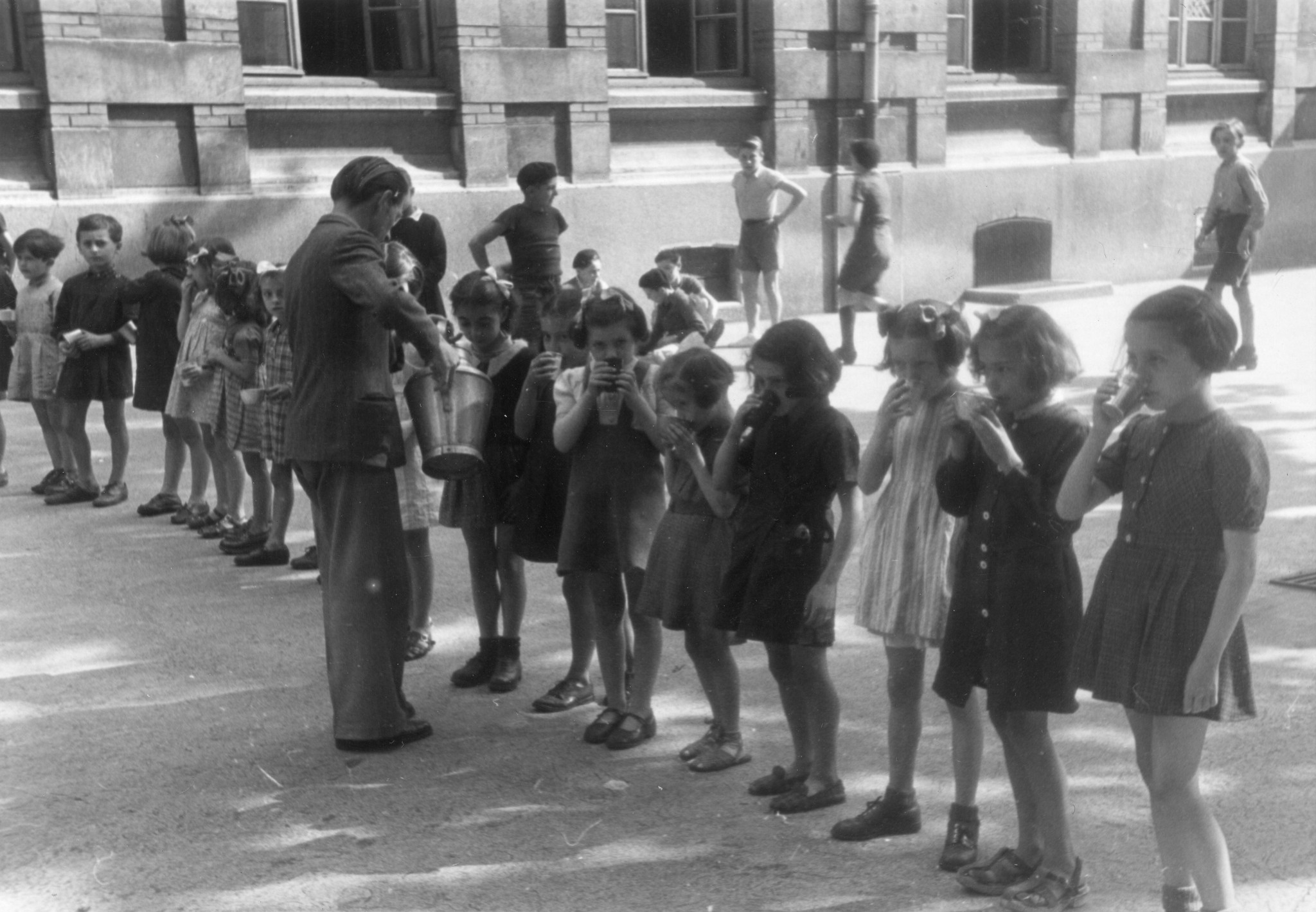 "Saint-Etienne, 1945. Mit grossere Hingabe verteilen die Lehrer und Lehrerinnen täglich in einer Pause ihren deficienten Schülern eine Tasse "Don Suisse"-Milch."