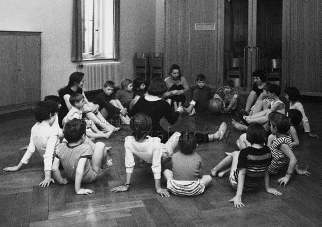 Turnen - Kinder sitzen bei einer Übung mit einem Ball am Boden; um 1970