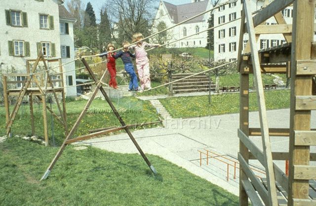 "Pausenhof Töss, Richterswil" - Drei Kinder balancieren über ein Seil; um 1975