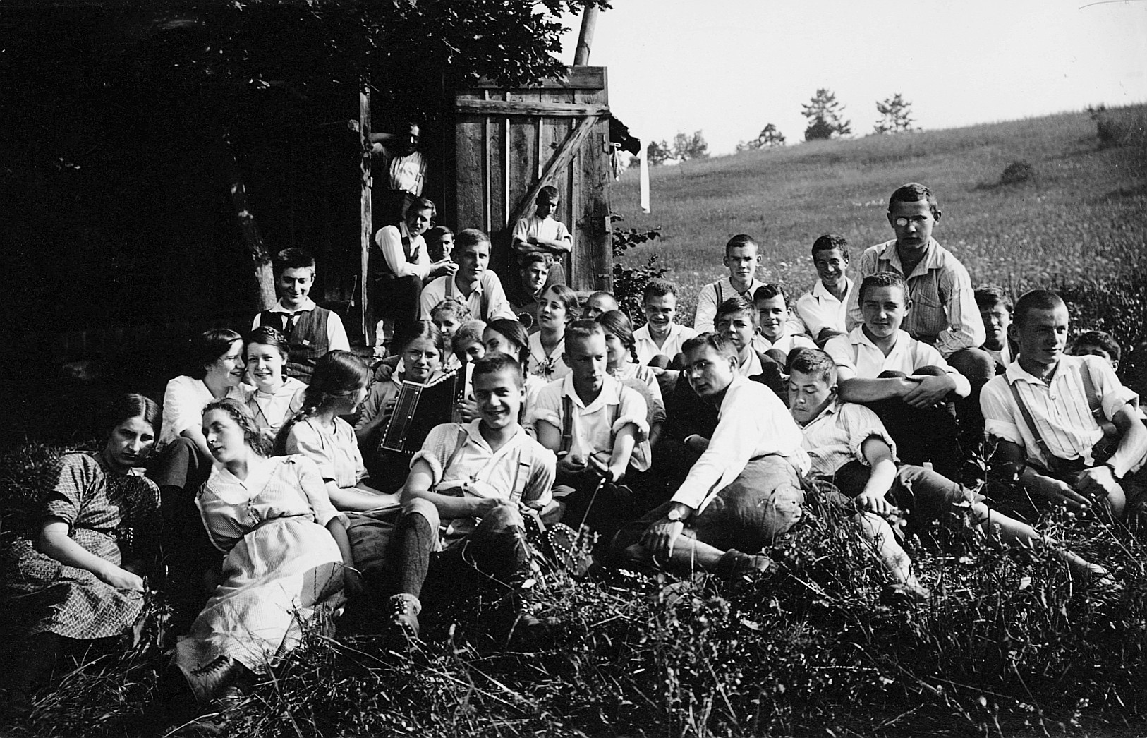 Wandervögel der Ortsgruppe Zürich (OG Turicum) sitzen auf der Wiese beim Meilener Hüttli, ein Mädchen Akkordeon spielend (Sonnenwend
