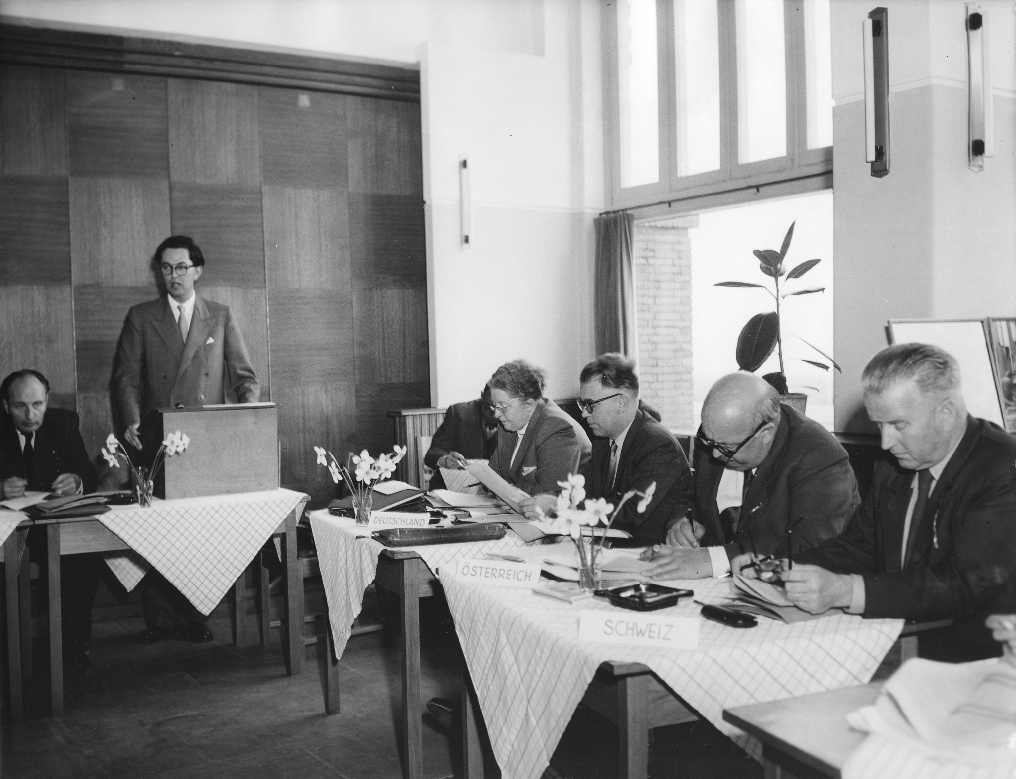 Zusammenkunft der Mitglieder des Internationalen Arbeiterhilfswerk, die Parteien sitzen in einem Kreis; ein Mann hält eine Rede