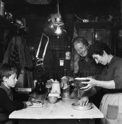 Zwei Frauen beim Backen, ein Knabe sitzt am Tisch und liest; um 1965
