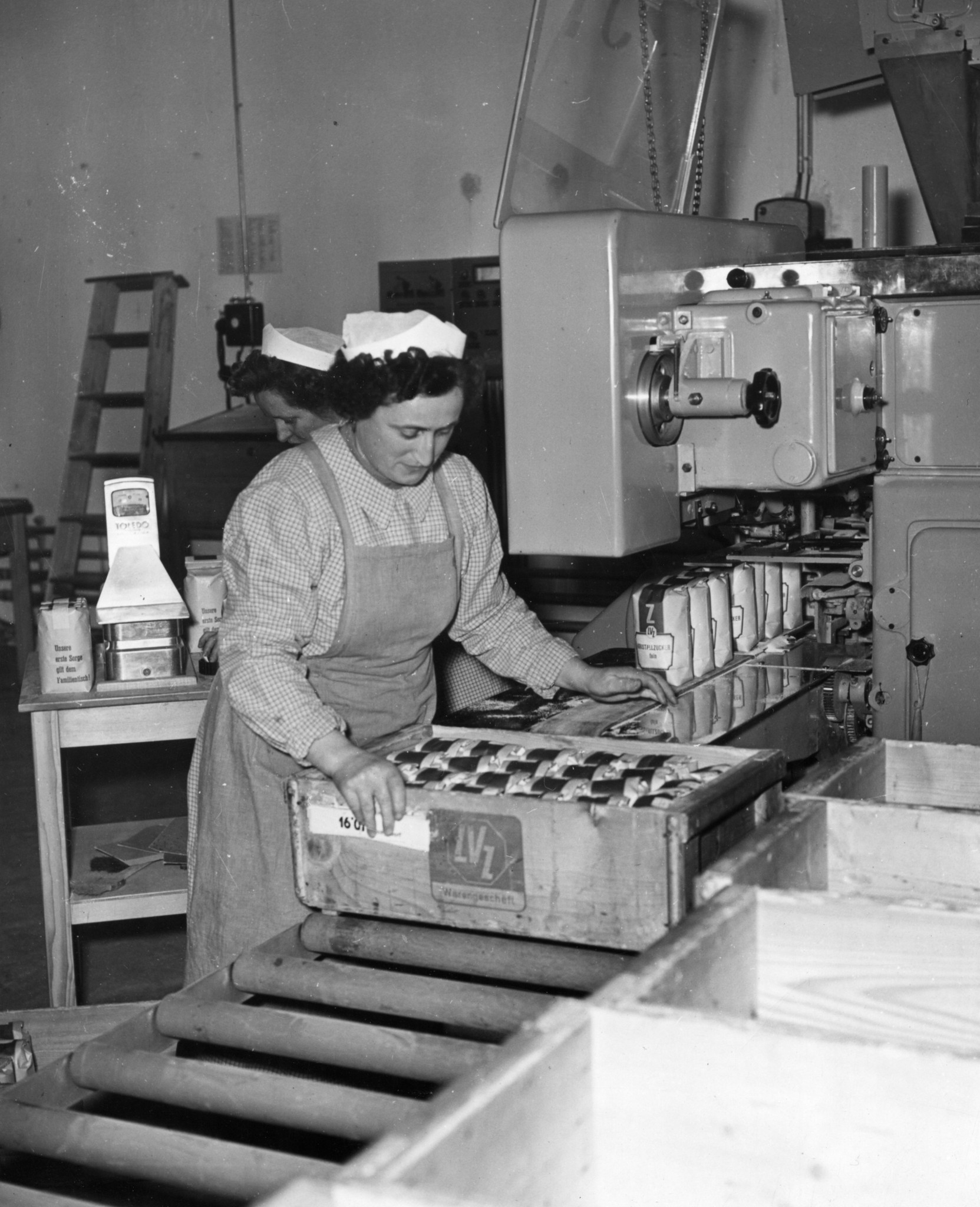 Frau an einem Transportband verpackt Zuckerpackungen in eine Kiste