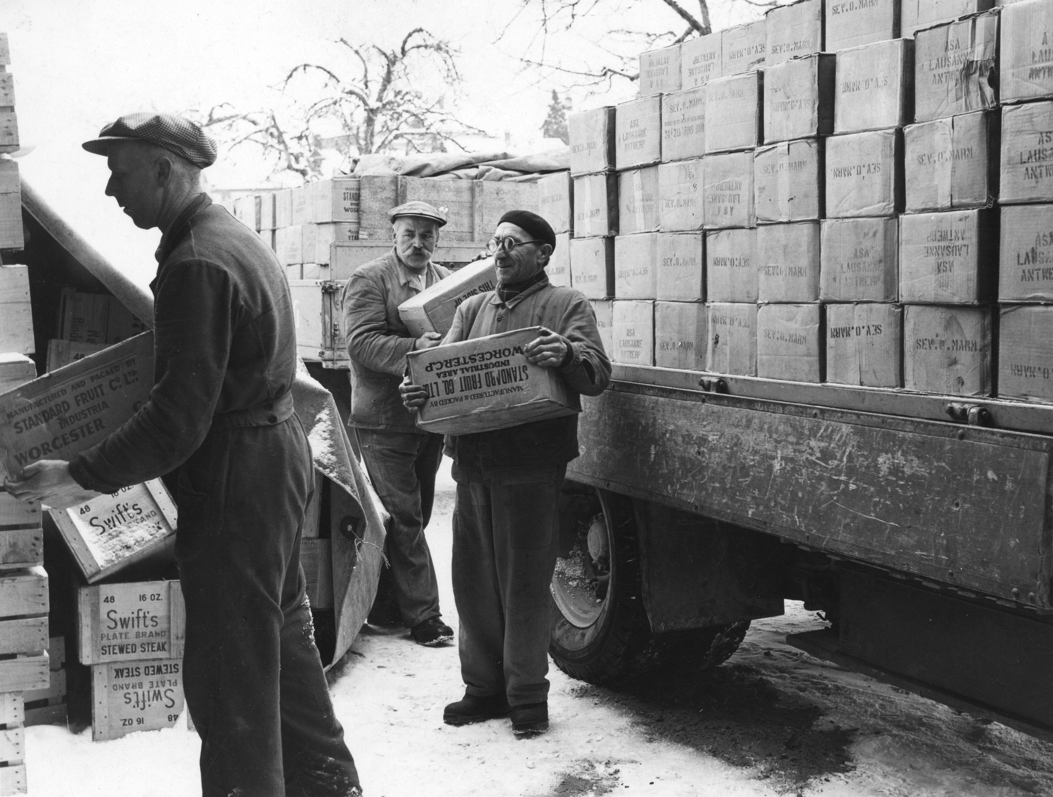 "Ankunft von ausländischen Konserven", drei Männer beim Abladen von einem Lastkraftwagen mit Lebensmittelkartons ("Manufactured and packed by Standard Fruit co. ltd. industrial area Worcester c.p", [aus Grossbritanien])