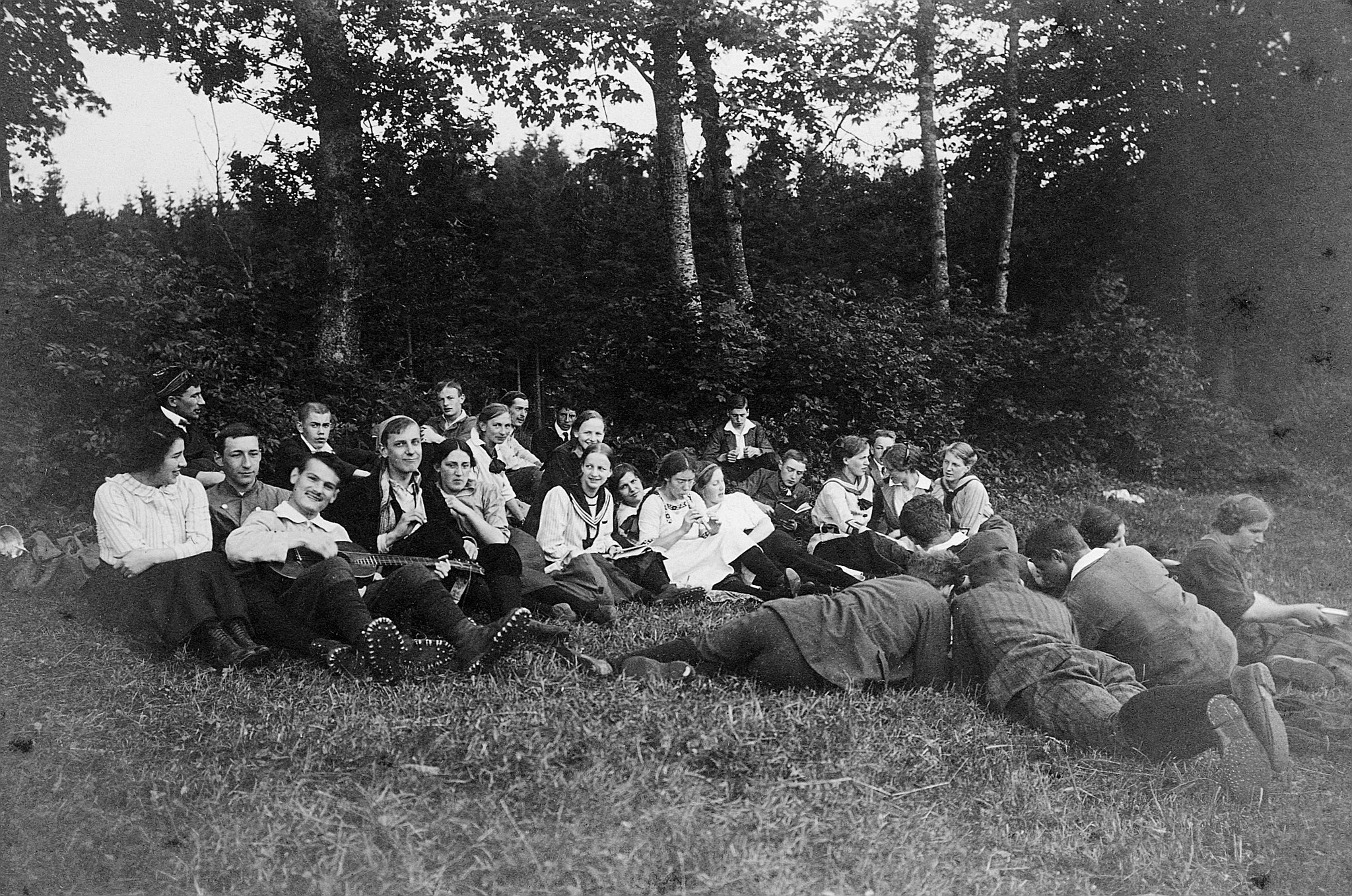 Wandervögel sitzen auf der Wiese am Rand eines Wald; ein Wandervogel Gitarre, ein Wandervogel Blockflöte spielend (1914)