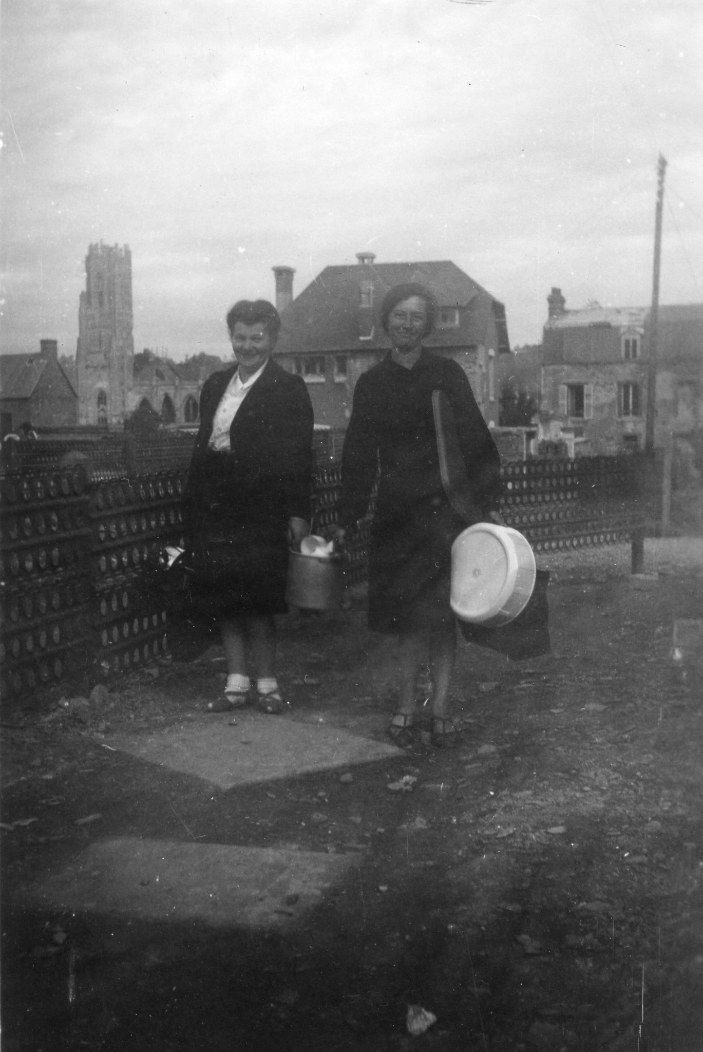"Verteilung von Geschirr und Geräten an die Bevölkerung von St.-Lô"; zwei Frauen mit Haushaltsutensilien