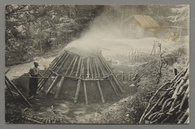 Köhler mit Schaufel neben rauchendem Kohlenmeiler, um 1930
