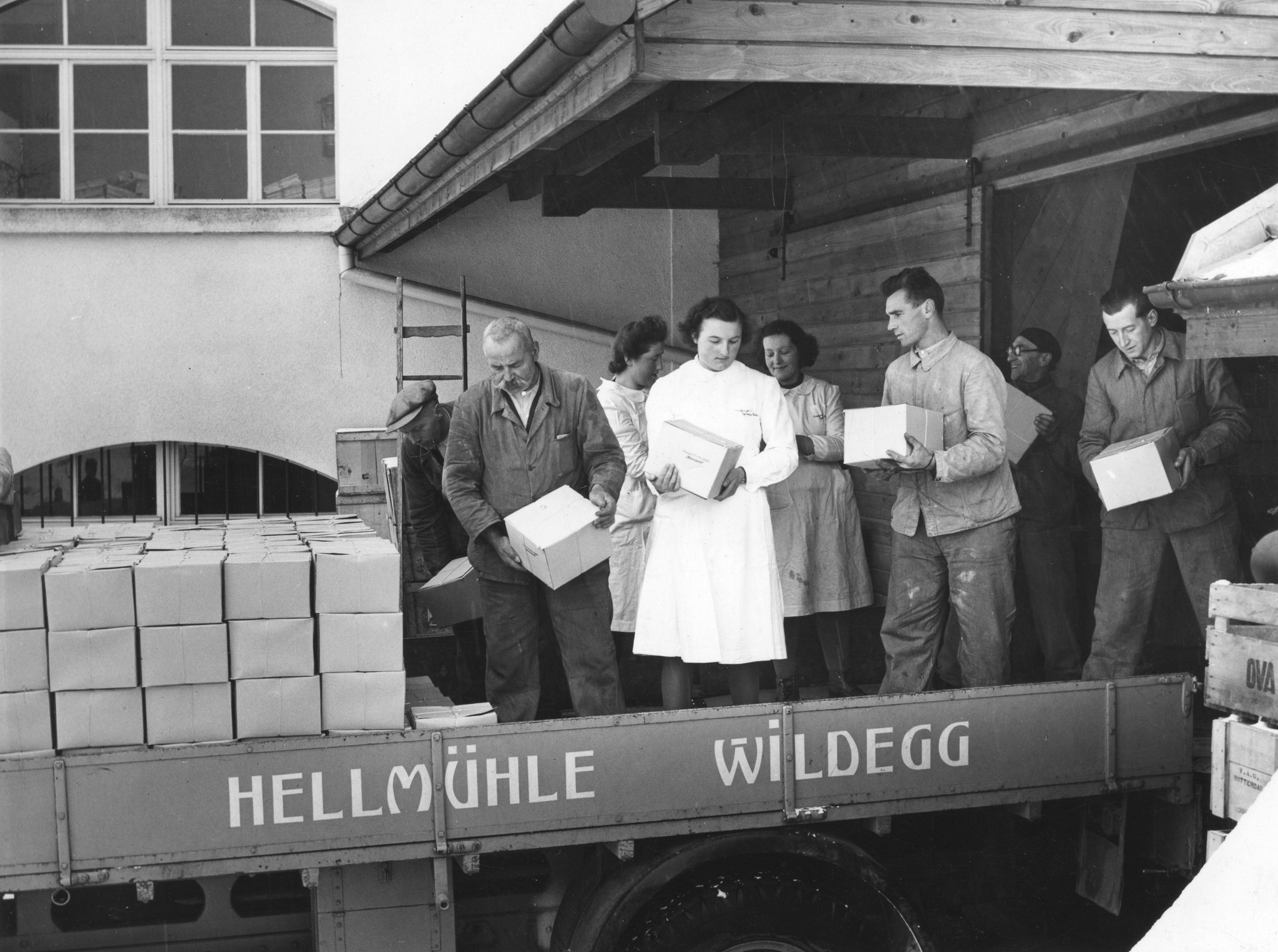 "Schweiz: Verladen der Colis"; Männer und Frauen verladen die Kartonkisten auf einen Kleintransporter mit der Aufschrift "Hellmühle Wildegg"