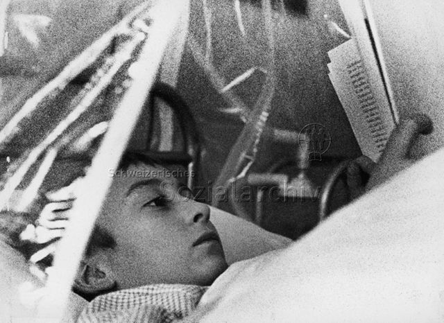 "Kinderheilstätte Davos, Asthma-Therapie" - Ein Junge liegt bei einer Therapie im Bett und liest; 1972