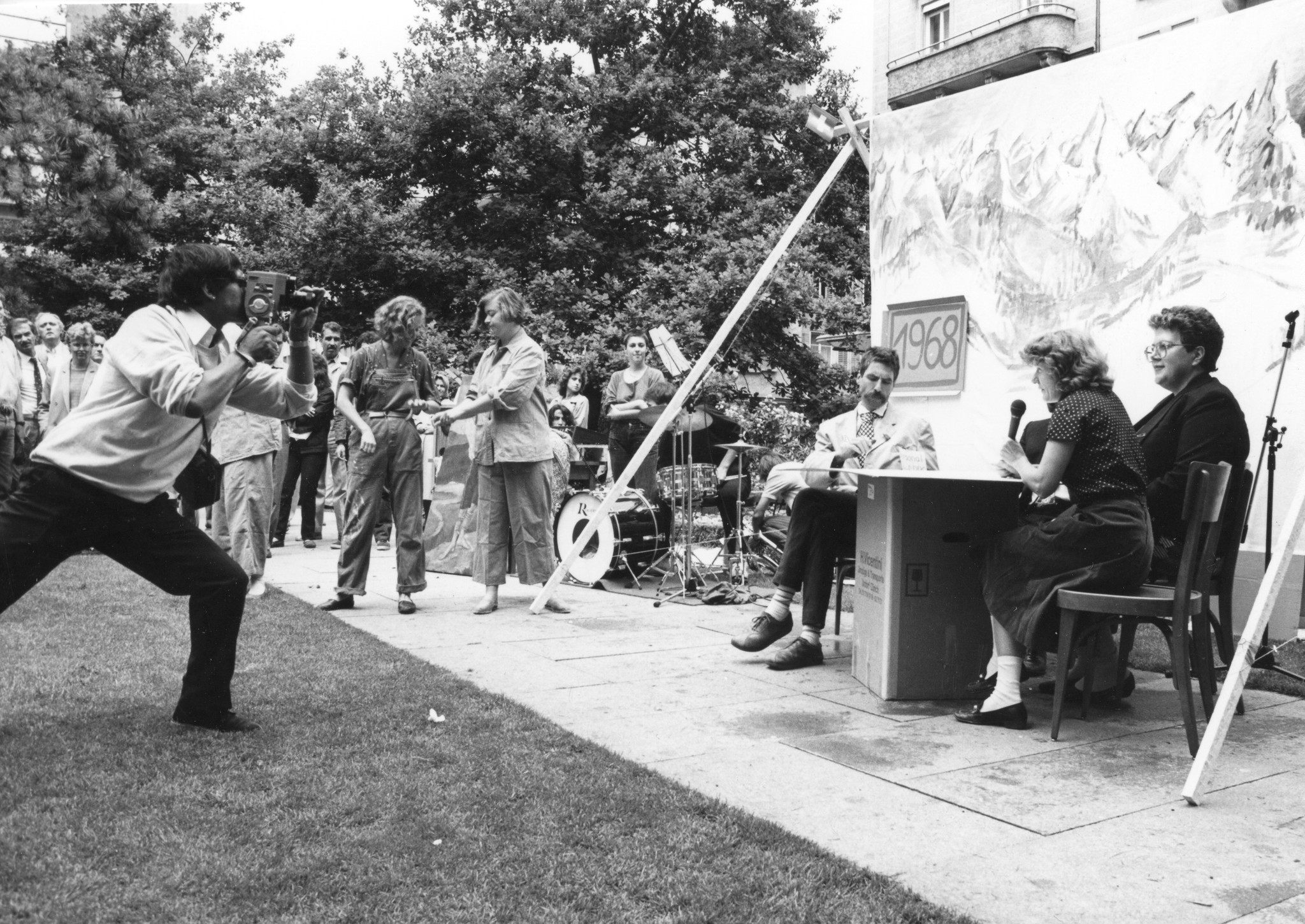 Tag des Flüchtlings 1984; auf der Pestalozziwiese sitzen drei Schauspieler vor einem Bergplakat und werden von einer Kamera gefilmt, vermutlich eine Theateraufführung des SAH