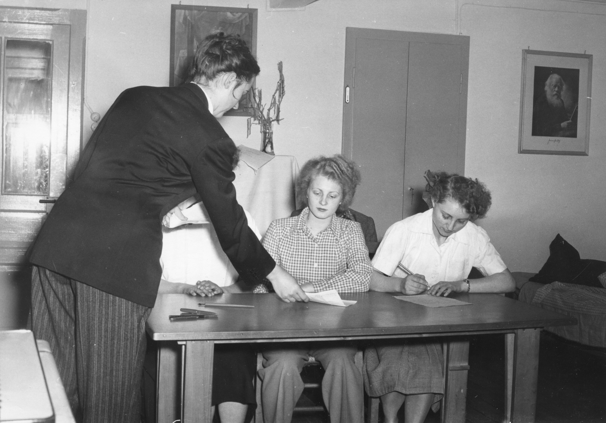 "Cavigliano - Haushaltungskurs für deutsche Flüchtlingsmädchen vom Dezember 1950 bis Februar 1951", Lehrerin beim Sammeln von schriftlichen Aufgaben, drei Schülerinnen