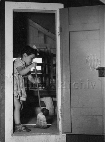 "'Useputzete' im Puppenhäuschen, Robinsonspielplatz Wipkingen, Zürich" - Ein Mädchen beim Wischen; um 1960