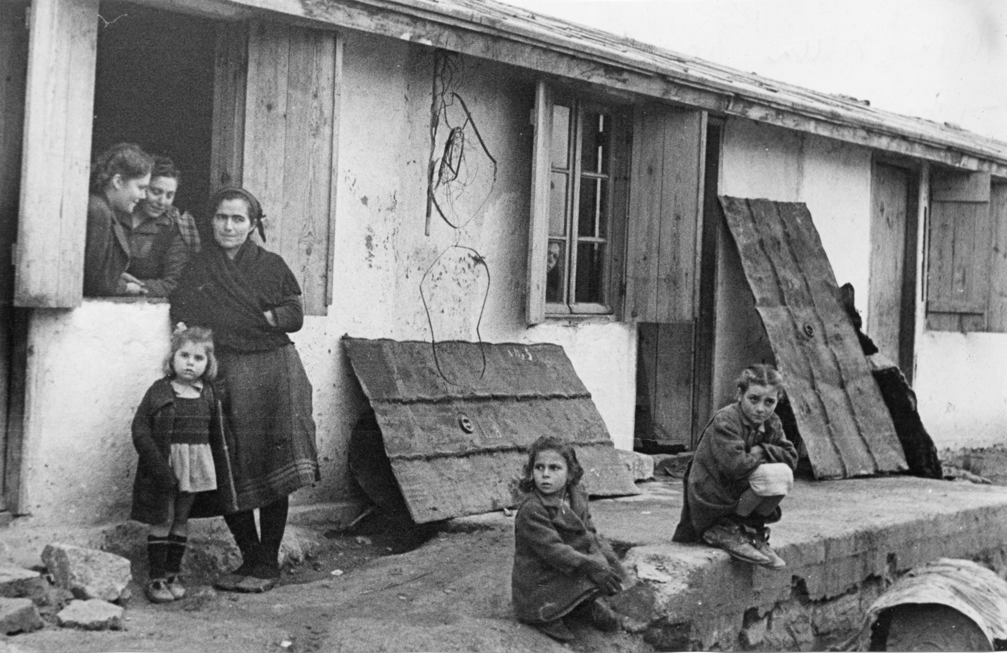 "Une maison du quartier Philippoupol (?), où sont installées des victimes des Andartès [Griechisch: Partisans/Partisanen] du village Keurger (?) de l'Olympe." Frau und Kinder in Elendsumgebung während des Griechischen Bürgerkrieges