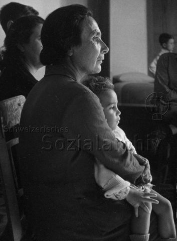"Mutter + Kind" - Kleinkind sitzt auf dem Schoss der Mutter; um 1965