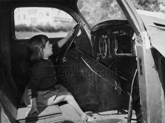 Spielplatz - Mädchen sitzt in einem alten Fahrzeug und spielt; um 1965