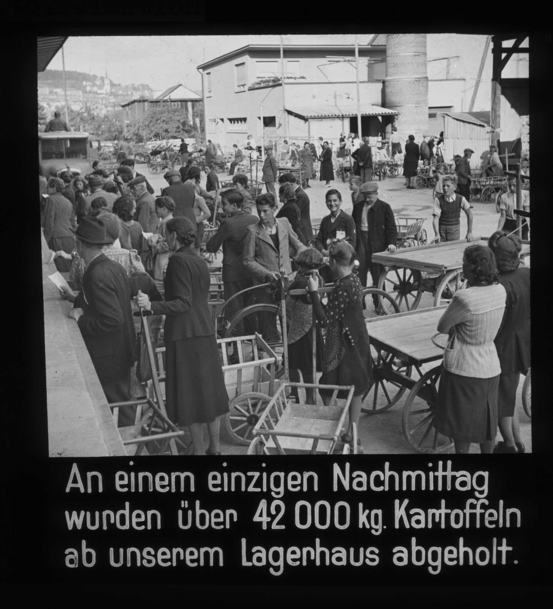 Dia: Lagerhaus-Rampe, davor wartende Leute mit Leiterwagen: "An einem einzigen Nachmittag wurden über 42000 kg Kartoffeln ab unserem Lagerhaus abgeholt."