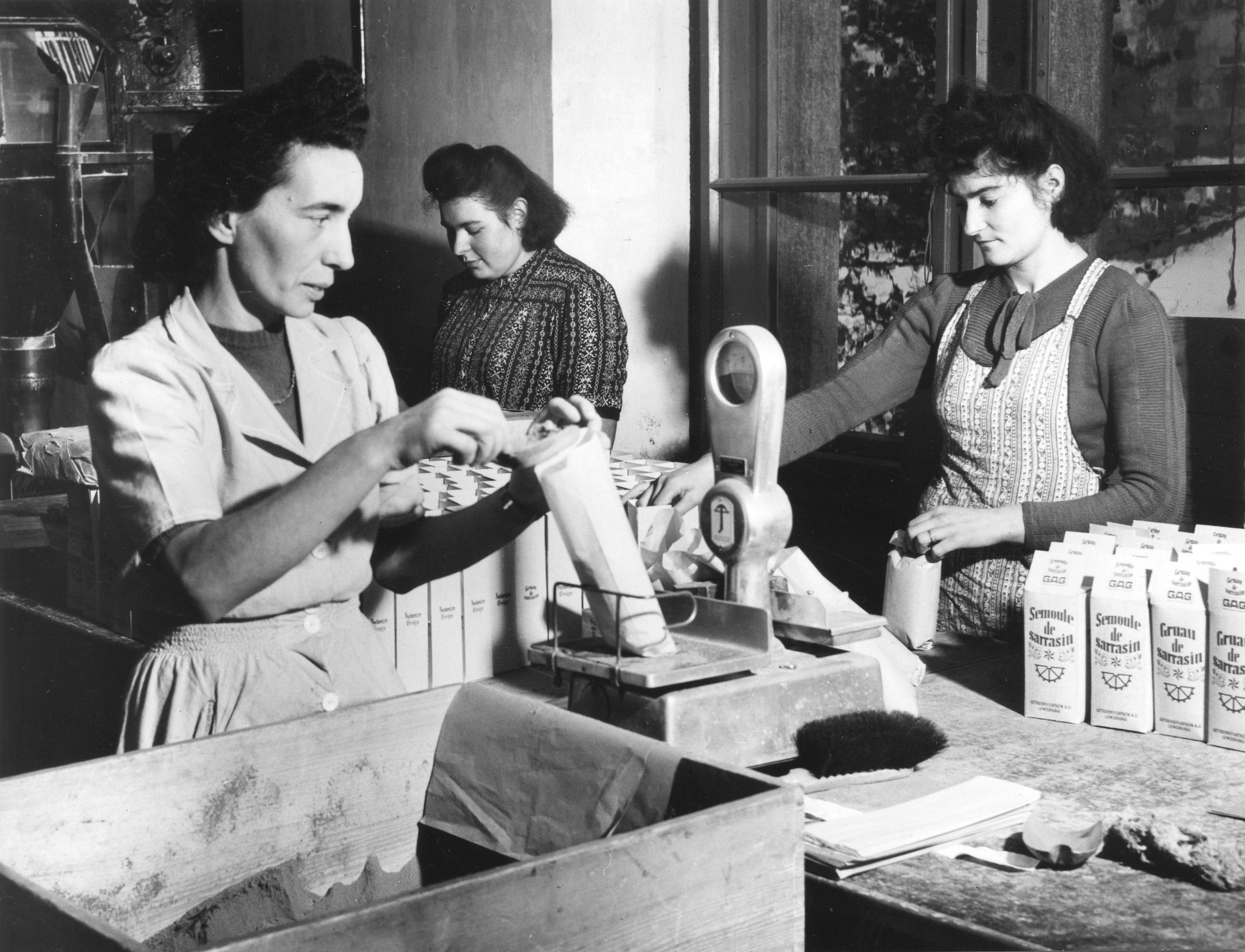 "Beim Abfüllen von Kakao für die Colis [suisses]", drei Frauen bei der Vorbereitung von Lebensmittelpaketen, um 1950 (Nachkriegszeit) (hier aber eher: Buchweizen)