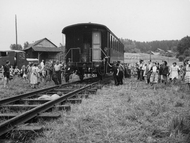 Leute schieben ein Bahnwaggon, Zuschauerinnen und Zuschauer rennen durch die Wiese, um 1965