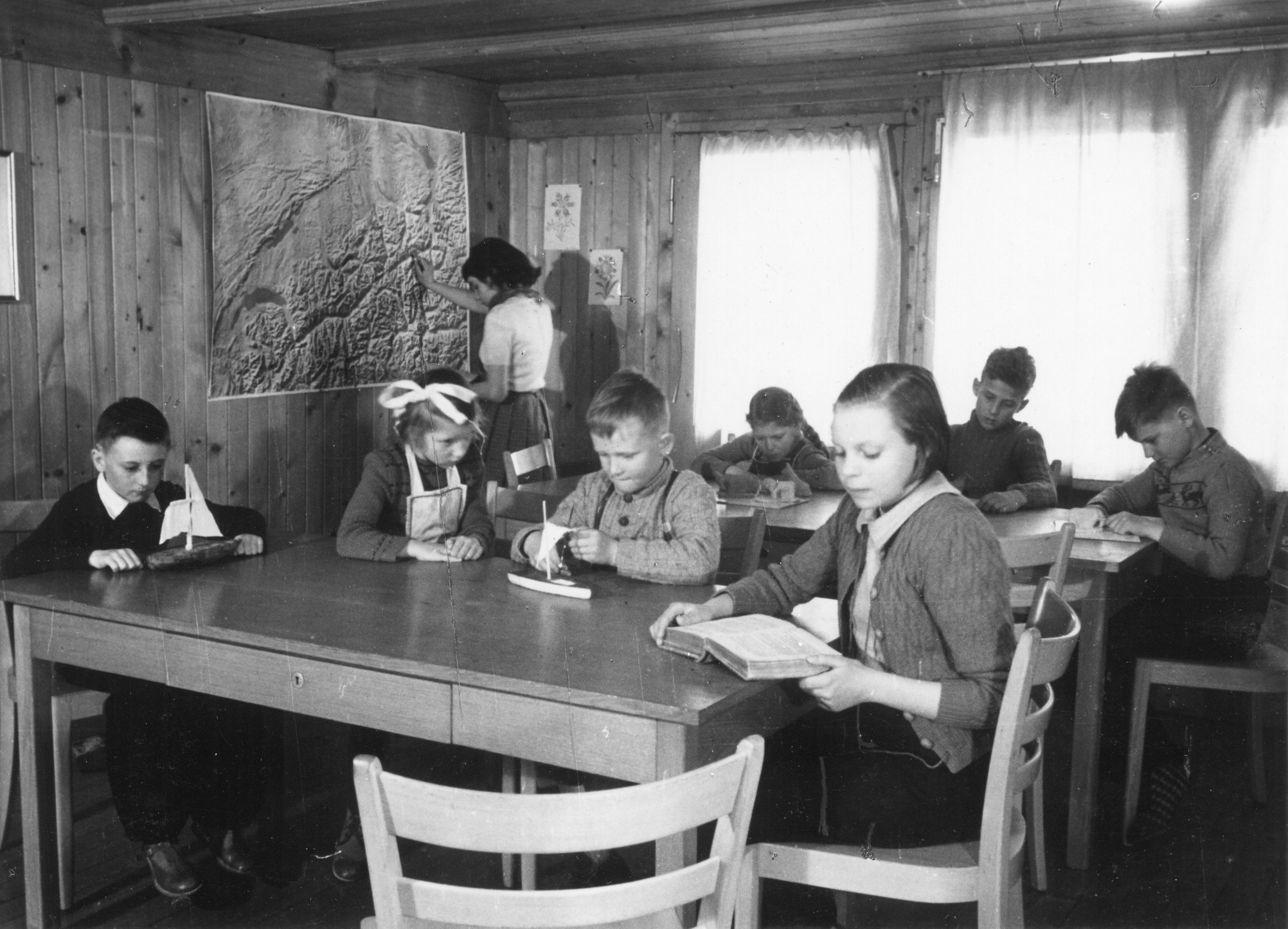 Vermutlich Kinder in einem Ferienlager: Kinder sitzen an Tischen und lesen überwiegend