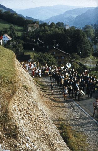 "Lichtensteig" - Marsch mit Marschkappelle entlang einer Strasse; um 1975