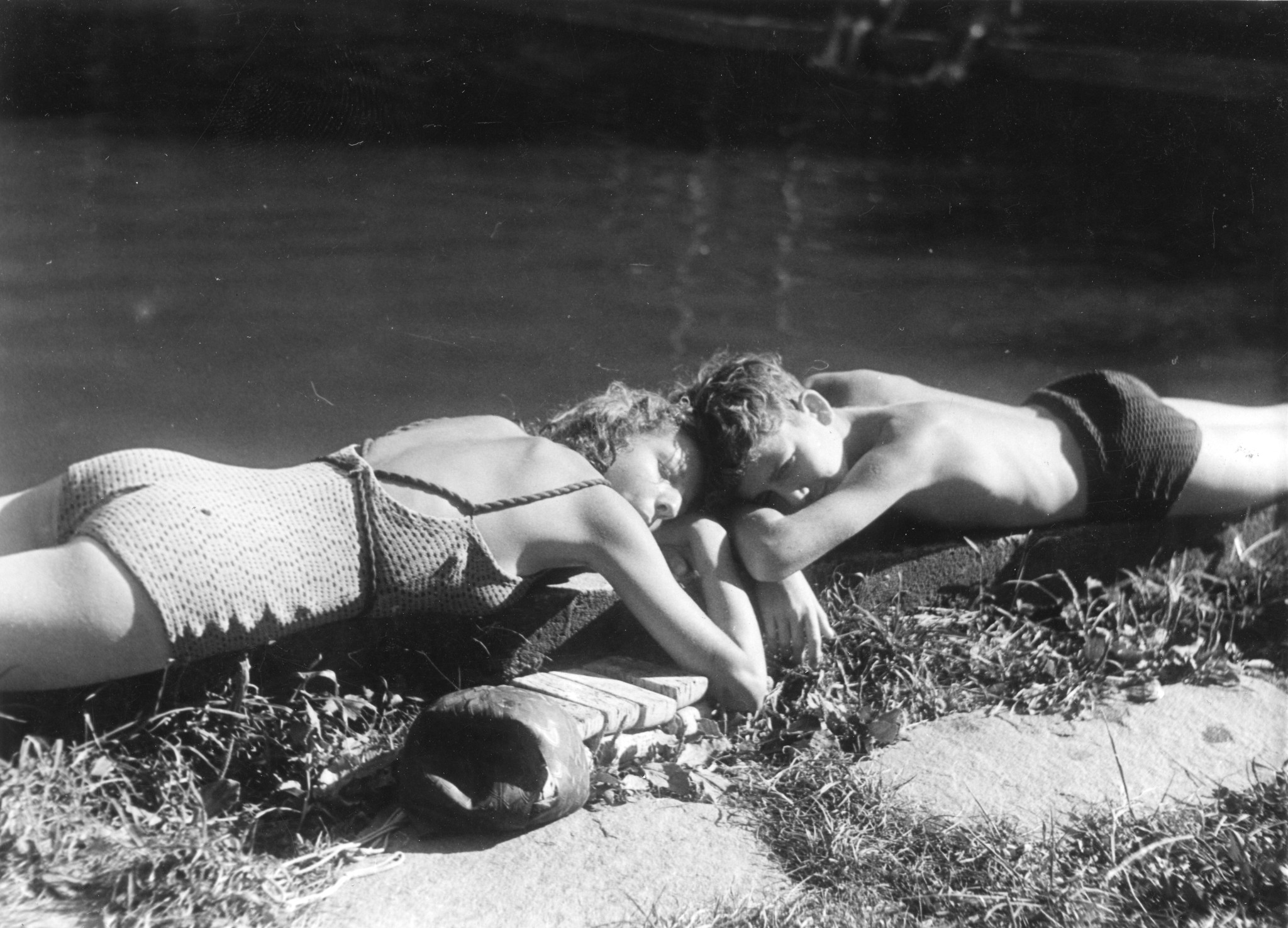 Ein Mädchen und ein Junge liegen am Wasser und sonnen sich