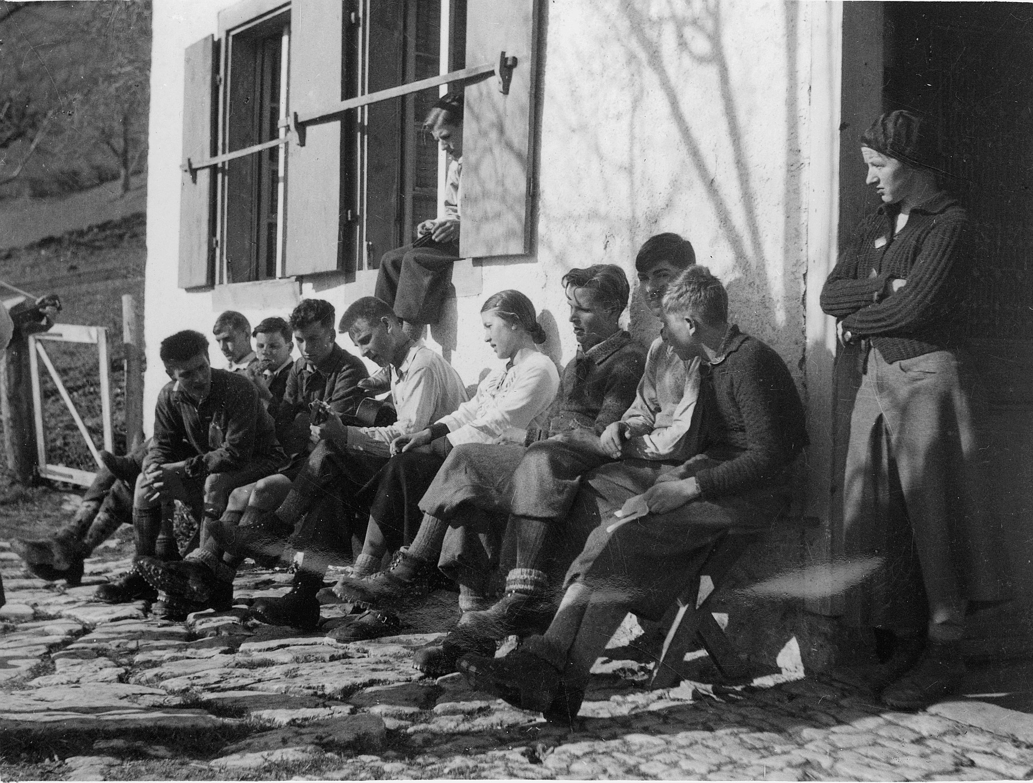 Wandervogeltreffen: Führertag Wohlen - Wandervögel sitzen auf einer Sitzbank vor einem Haus - Ein Wandervogel Gitarre spielend (ca.
