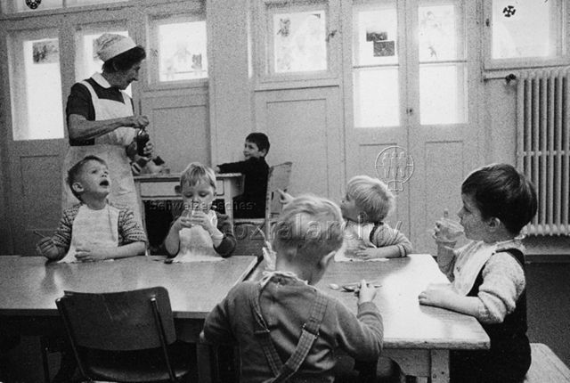 "Kinderheilstätte [Davos], Essen" - Kinder am Tisch, Krankenschwester bringt die Medizin; 1971