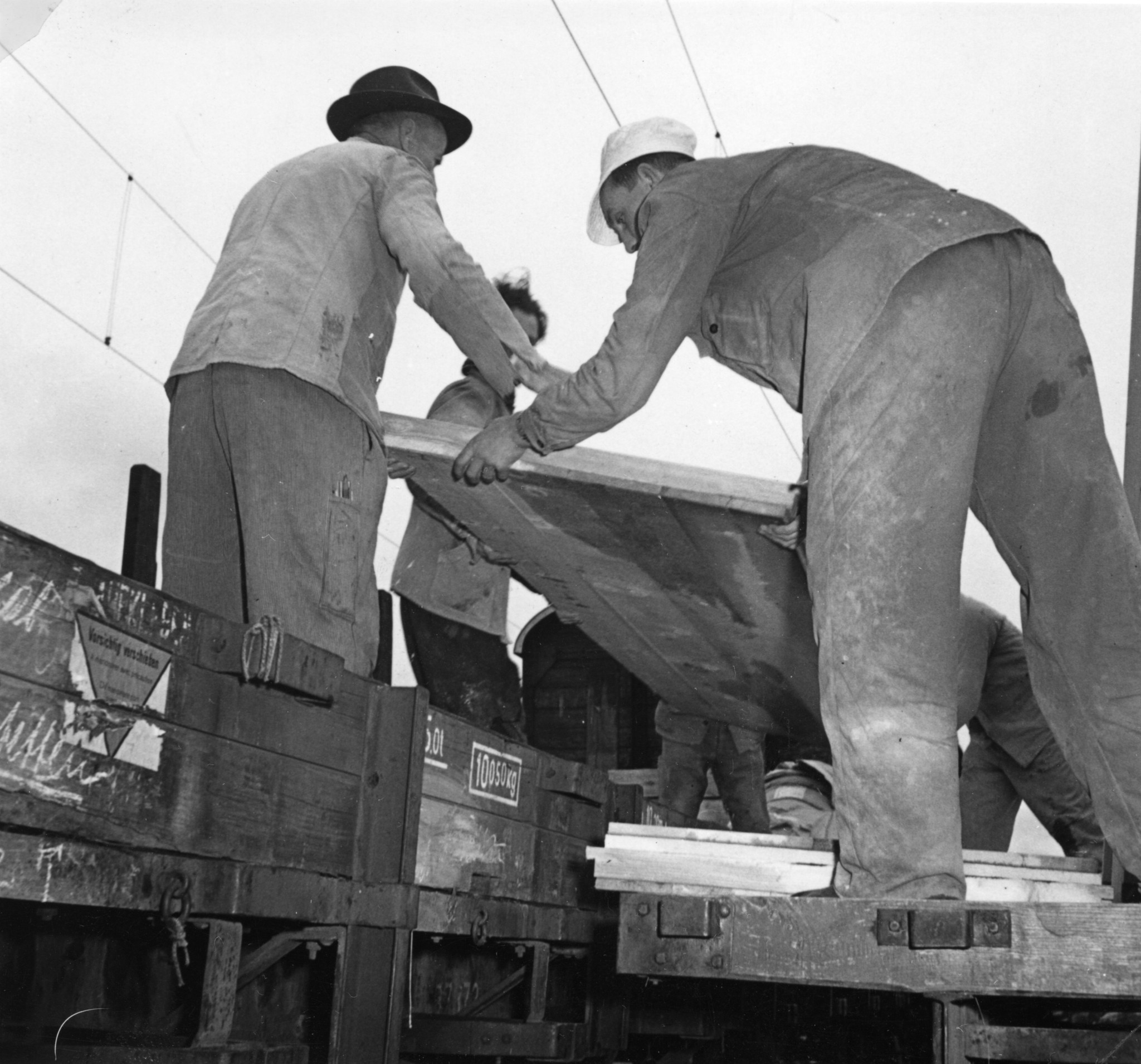 Tanklager / Hafen: Männer verladen Platten auf einen Eisenbahnwaggon