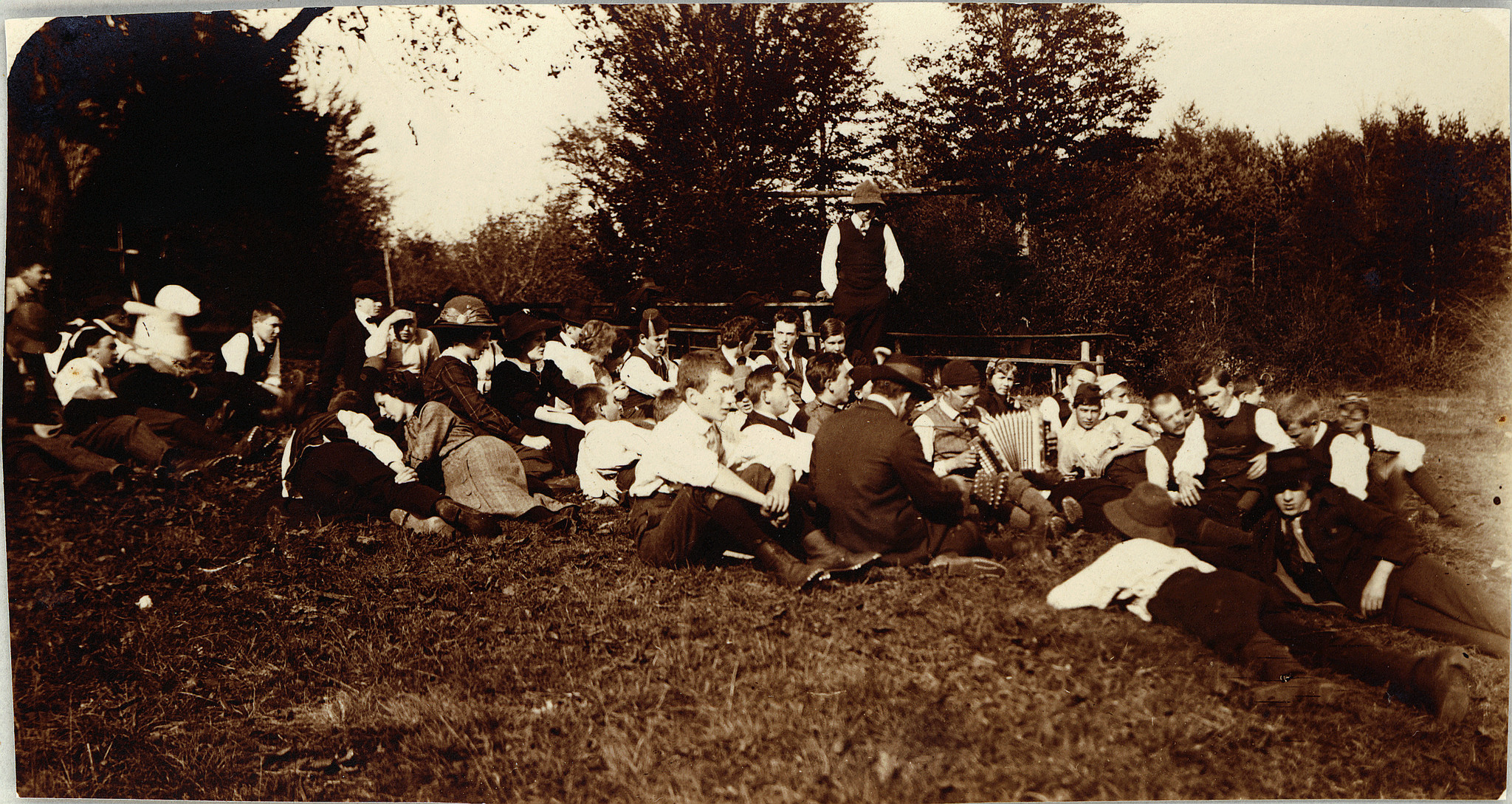 Versammelte Wandervögel auf der Wiese am Westschweizerischen Wandervogeltag in Magglingen - Ein Wandervogel Akkordeon spielend (1912