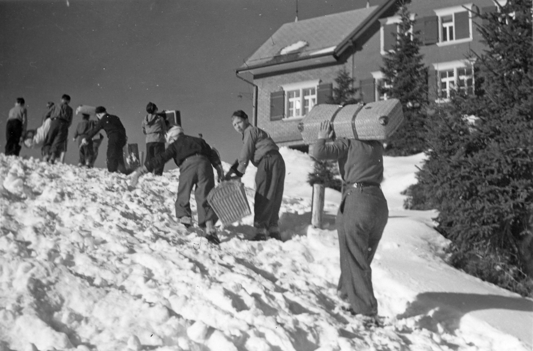 "Die Schneehasen"; Kinder tragen Gepäck einen schneebedeckten Hang hoch