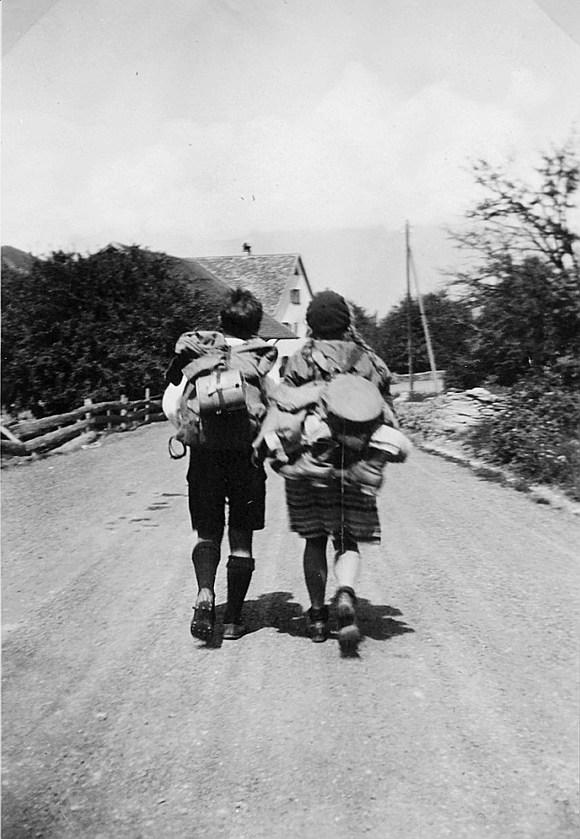 Bündner Sommerfahrt: Zwei Wandervögel mit Rucksäcken laufen auf einem Schotterweg (1930)