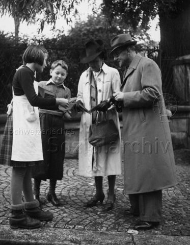 "Pro Juventute-Karten-Verkauf" - Zwei Kinder und zwei Erwachsene sehen sich Karten an; 1939