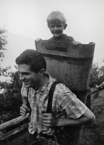 PraktikantInnenhilfe - Praktikant trägt einen kleinen Jungen in einer Bränte; 1966