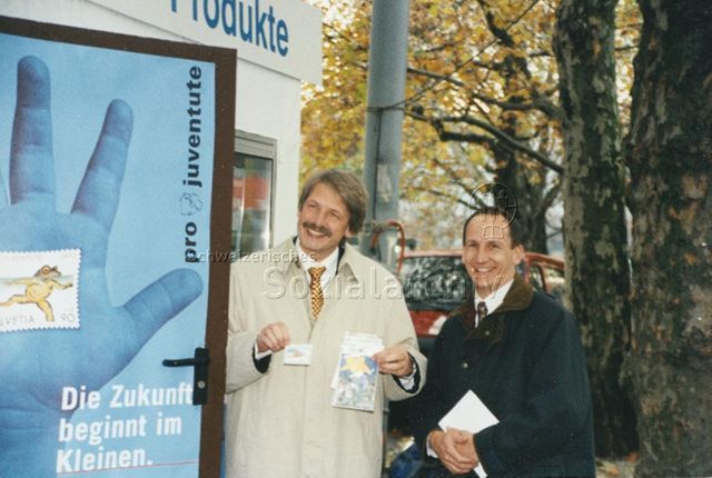 "Markenverkauf am Bellevue mit Zürcher Stadtpräsident Josef Estermann" - Herr Estermann präsentiert Marke und Karten, ein zweiter Herr steht daneben; 1997