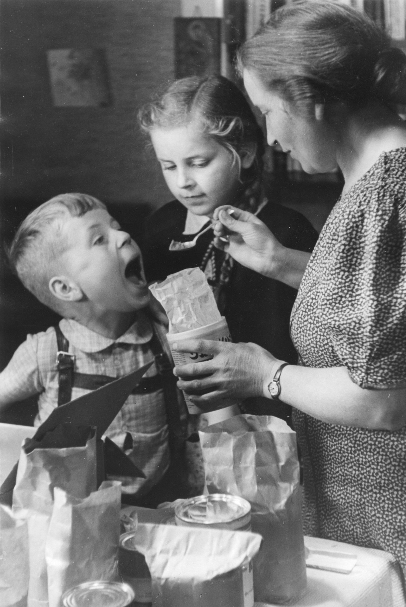 "Hamburg, Sommer 1948: ein Freipaket kommt an!"; die Mutter lässt den Jungen von den Lebensmitteln kosten (vermutlich Ovomaltine)