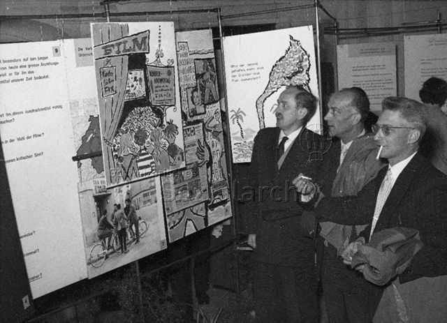Männer lesen Infoplakate; um 1960