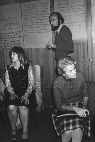 "TZI Kurs Bülach" - Mann steht vor Poster, vorne zwei Frauen auf Stühlen; 1976