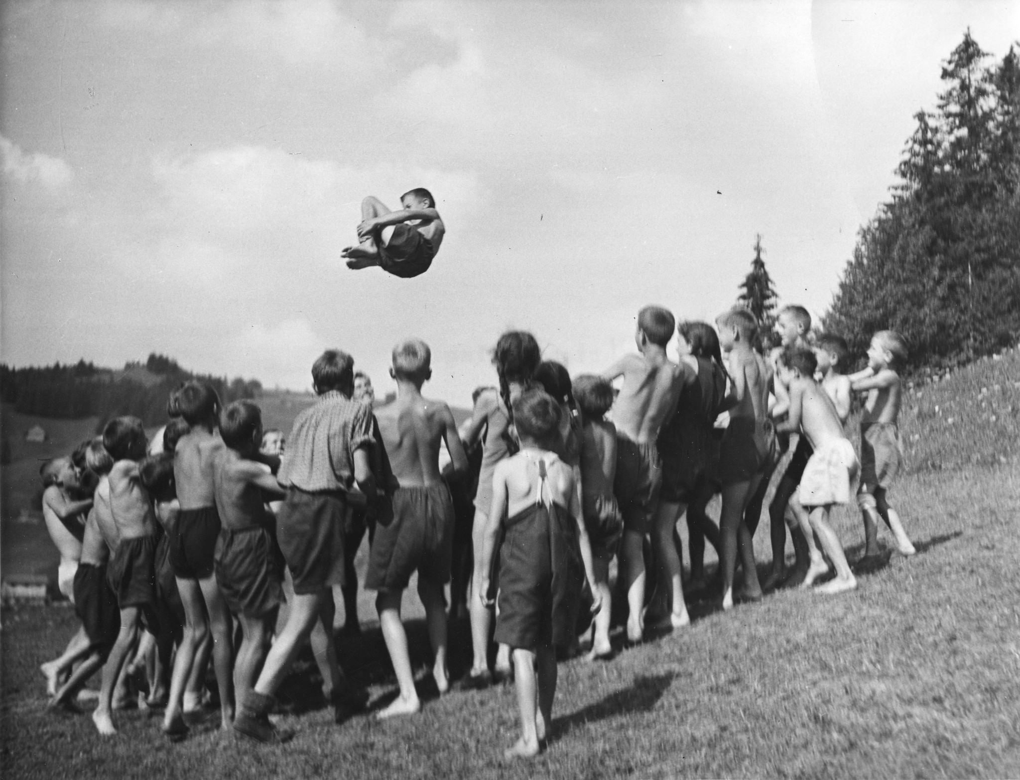 Ein kleiner Junge wird von einer Gruppe Kinder mittels Tuch in die Luft geworfen