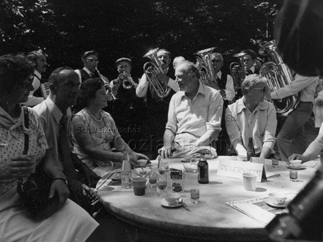 Bosco della Bella, Feriendorf für kinderreiche Familien, Jubiläum - Bundesrat Willi Ritschard im Gespräch mit unbekannten Personen, im Hintergrund spielt eine Kapelle; 1977