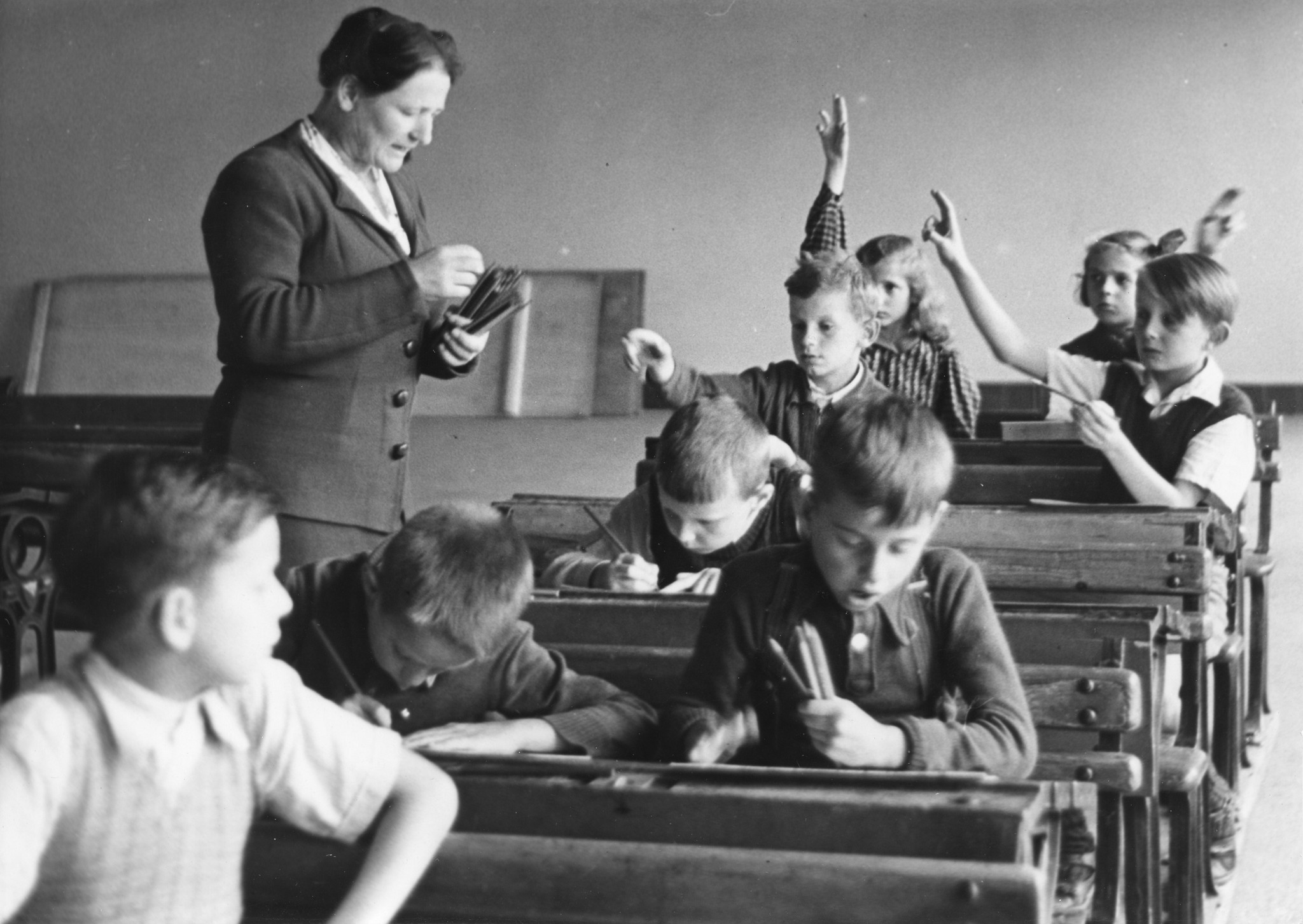 Lehrerin beim Verteilen von Bleistiften und Schüler beim Schreiben, vermutlich in Zürich 1946