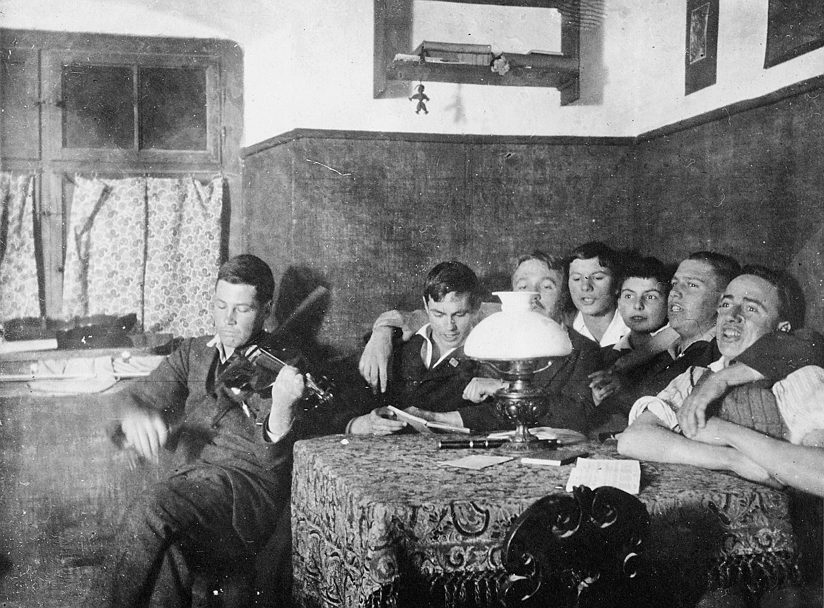 In der Bude: Wandervögel sitzen am Tisch und singen, ein Wandervogel Geige spielend (1918)