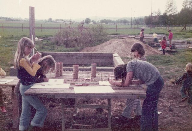 "Robi Therwil" - Mädchen zeichnen, im Hintergrund Kinder beim Spielen; 1976