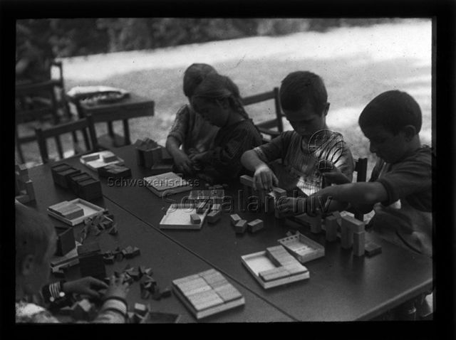Diaserie zum Thema Kindergarten; Kinder sitzen an einem Tisch und spielen mit Holzklötzen; um 1930