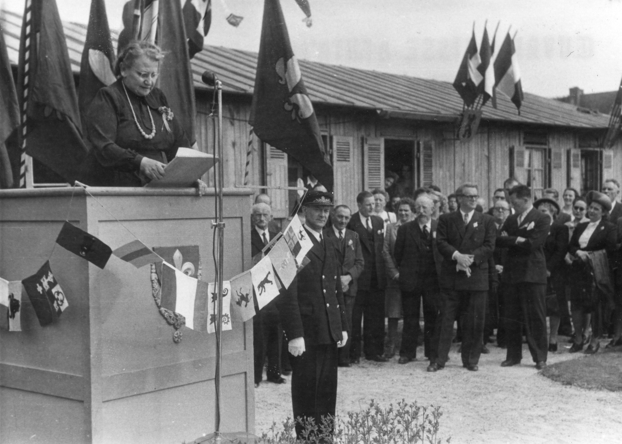 Regina Kägi-Fuchsmann auf einem Podest eine Rede haltend, Denis Cardonnier und weitere Personen im Hintergrund zuhörend