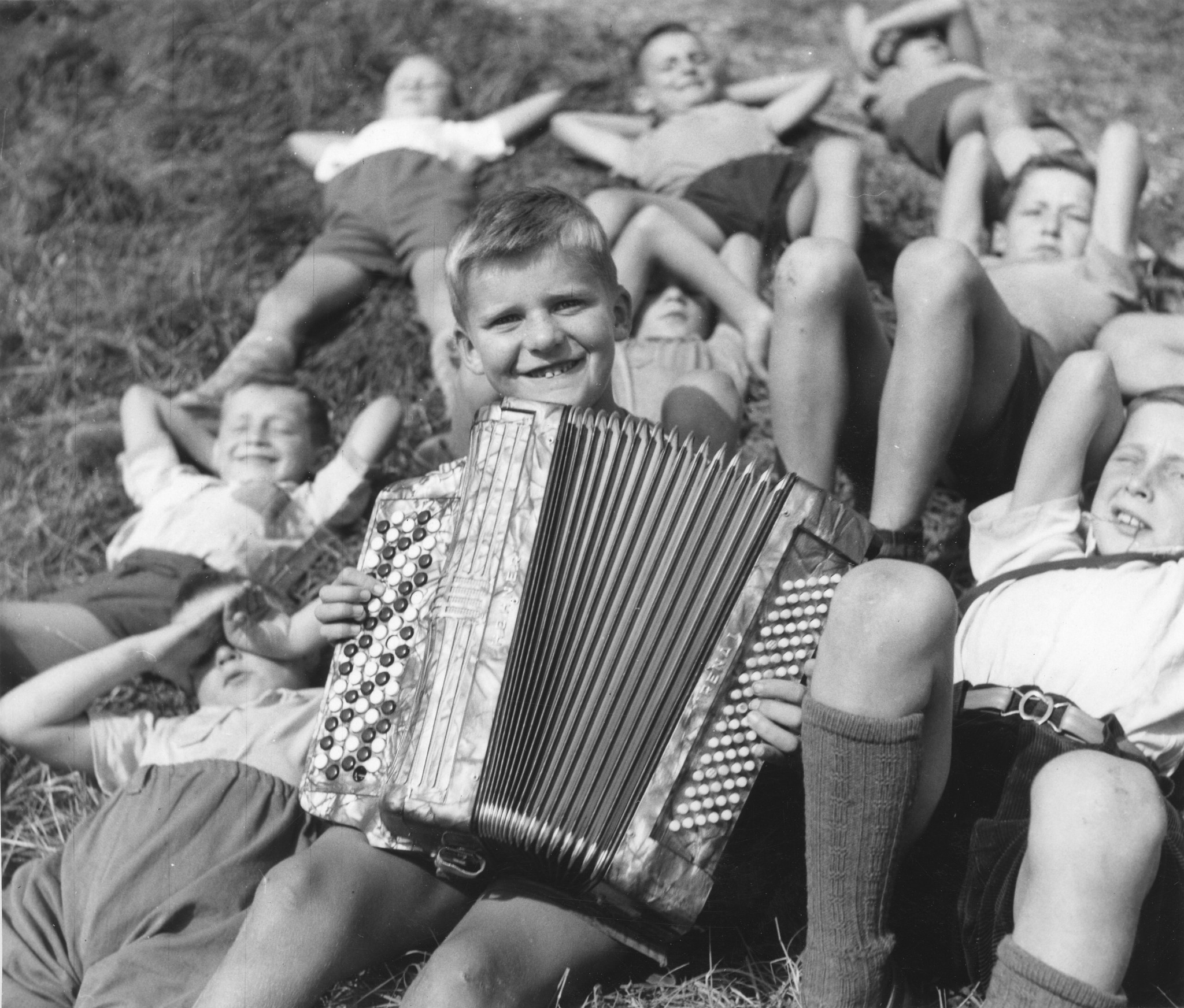 Ferienkolonie Landmark: Ein Knabe spielt Handorgel und die restlichen Jungen liegen zufrieden auf der Wiese