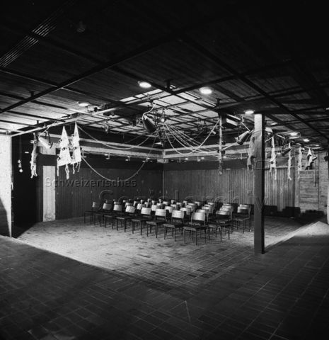 "Freizeitanlagen, Gemeinschaftszentren: Mehrzwecksaal Gemeinschaftszentrum Loreto Zug" - Raum mit Plattenboden, Stühle stehen unter der Deckenbeleuchtung; um 1970